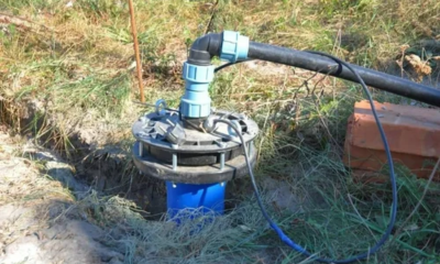 A pump tied to a pipe in the grass supplying water to the agricultural land needs repair services.